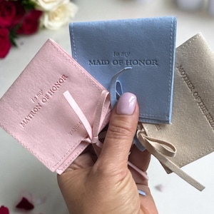 May include: Three small, fabric gift bags with satin ribbon ties. The bags are pink, blue, and beige. The bags are labelled "to my Matron of Honor", "to my Maid of Honor", and "Mother of the Bride".