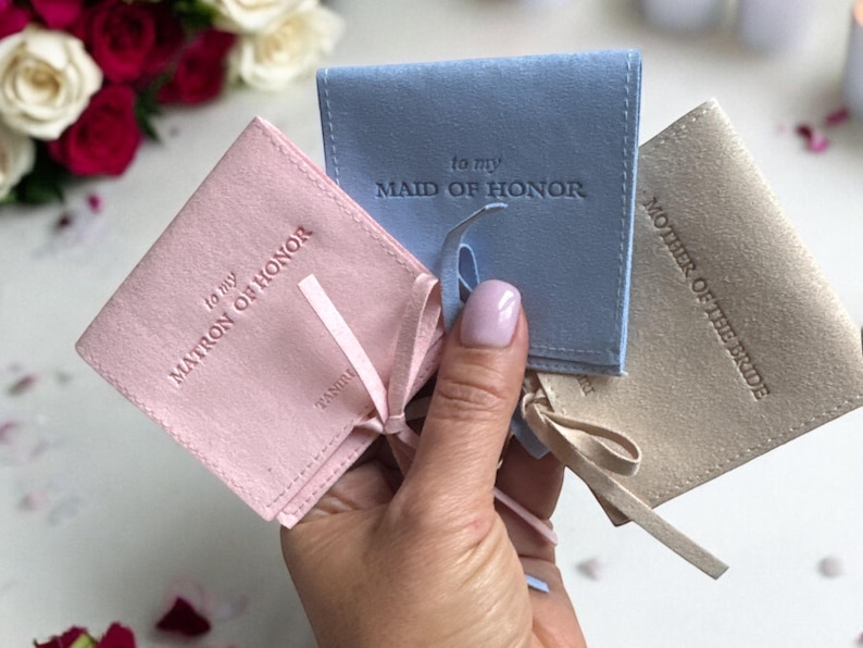 May include: Three small, fabric gift bags with satin ribbon ties. The bags are pink, blue, and beige. The bags are labelled "to my Matron of Honor", "to my Maid of Honor", and "Mother of the Bride".