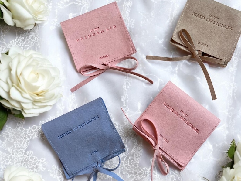 May include: Four small, fabric gift bags with satin ribbon ties. The bags are in blue, pink, and beige. Each bag has a different inscription: "To my Bridesmaid", "To my Maid of Honour", "To my Matron of Honour", and "Mother of the Groom".