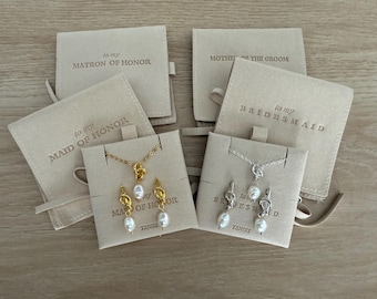 May include: Jewelry sets with necklaces and earrings, featuring pearl pendants and knot designs. The sets are presented on cards and accompanied by beige pouches with text that reads "to my Matron of Honor", "Mother of the Groom", "to my Maid of Honor", and "to my Bridesmaid".