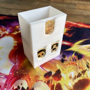 May include: White plastic storage box with three compartments. The compartments hold small, round, gold-colored tokens with black and white designs.