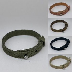 Op de afbeelding: Vijf leren armbanden in verschillende kleuren: olijfgroen, zwart, beige, roze en bruin. Elke armband heeft een getextureerd oppervlak, een lus sluiting en een zilverkleurige metalen knop. De armbanden worden gepresenteerd tegen een witte achtergrond.