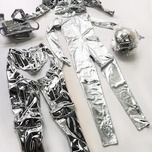 May include: A futuristic silver costume set, including a jumpsuit, shoulder pads, pants, and a vest. The metallic material reflects light, creating a shiny appearance. A silver ball wrapped in plastic is also included.