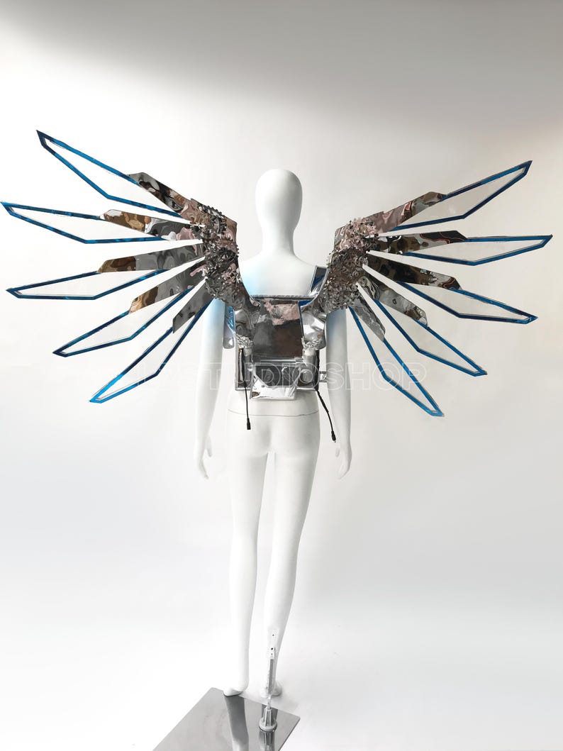 May include: A futuristic silver and blue wing costume displayed on a white mannequin. The wings have a layered design with reflective surfaces and blue trim. The costume is designed to be worn on the back.