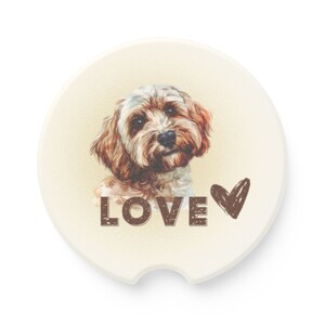 May include: A round, beige coaster with a brown watercolor illustration of a dog. The dog has brown and white fur and is looking at the camera. The text "LOVE" is printed in brown below the dog, and a brown heart is to the right of the text.