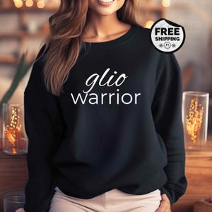 May include: Black crewneck sweatshirt with the text "glio Warrior" in white script. The sweatshirt has long sleeves and a classic design. A "Free Shipping" sticker is visible on the upper right.