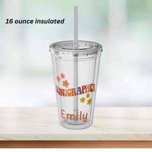May include: A clear 16-ounce insulated tumbler with a lid and straw. The tumbler features the word "SONOGRAPHER" in a retro font, the name "Emily", and floral accents in orange, purple, and yellow.
