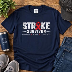 Peut inclure: Un t-shirt bleu marine à manches courtes avec le texte blanc vieilli STROKE SURVIVOR, où un ruban de sensibilisation rouge remplace la lettre O. Sous le texte, les mots STRONGER, WISER et STILL HERE sont imprimés en blanc.