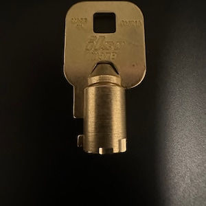 May include: A gold-colored key with a brass-colored barrel. The key has the text "Ilco 187B" and "MADE IN TAIWAN" on it.