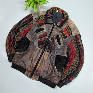 Puede incluir: Chaqueta de cuero marrón vintage con diseño patchwork. La chaqueta tiene cuello, puños y bolsillos negros. Las mangas tienen una tela estampada colorida con detalles en rojo, verde y amarillo. Cierre de cremallera.