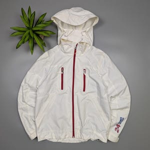May include: White hooded jacket with a red zipper and two red zippered pockets. The jacket has the text "24 Heures Du Mans" printed on the sleeve. The jacket is made of a lightweight material.