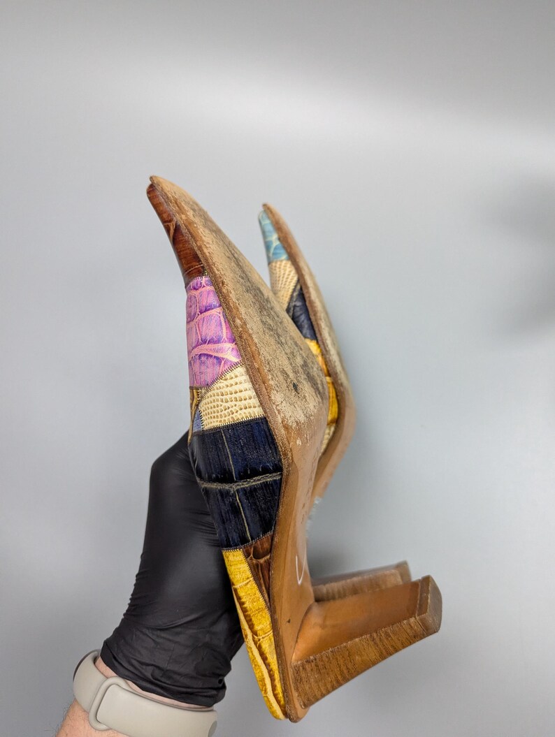 May include: A pair of high-heeled shoes with a patchwork design. The shoes feature a variety of colors, including brown, yellow, purple, and blue. The heels are made of wood.