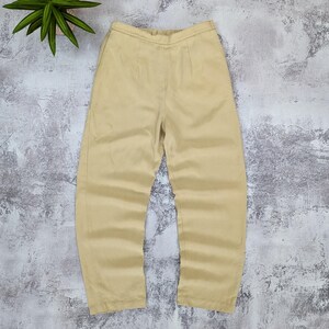May include: A pair of solid light tan trousers featuring a high-waisted design with an elasticized waistband, a straight-leg cut, and subtle vertical seam detailing running down the front of each leg, presented in a clean and simple style.