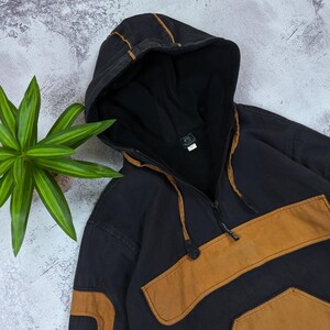 Pode incluir: Um moletom com capuz preto com fecho de meio z&iacute;per, um bolso frontal grande e pain&eacute;is de tecido na cor castanho nas mangas e no peito. O capuz inclui um cord&atilde;o com travas pretas e o interior &eacute; forrado com tecido preto.