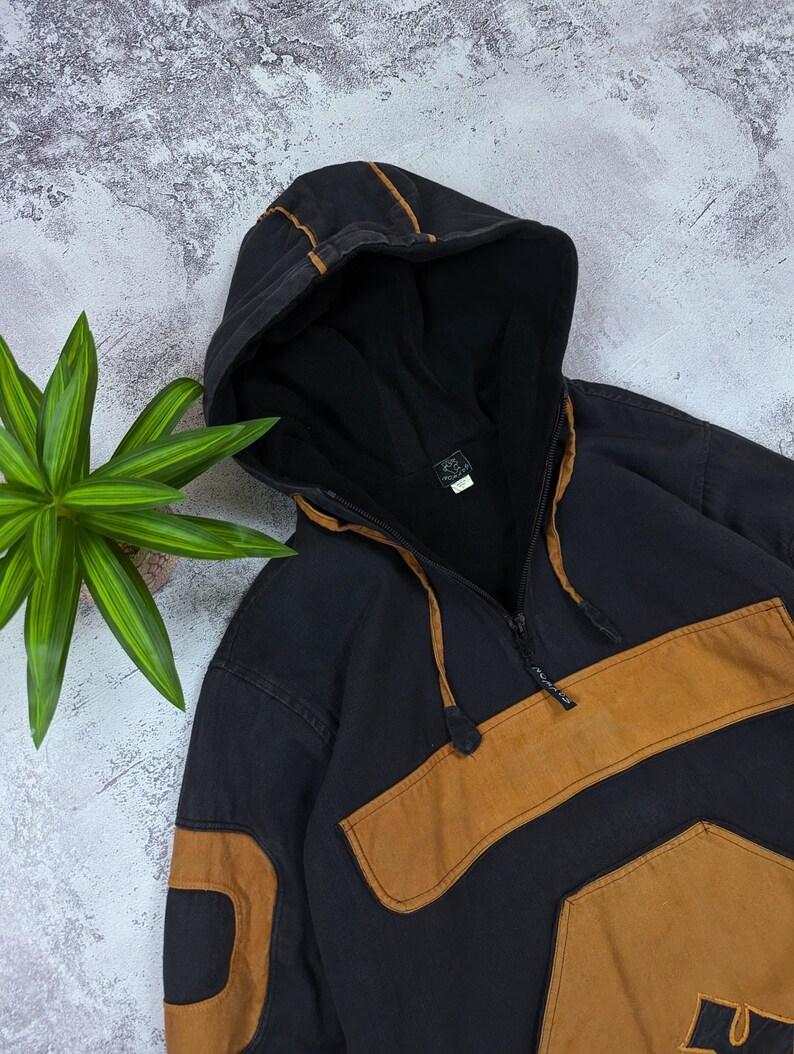 Pode incluir: Um moletom com capuz preto com fecho de meio z&iacute;per, um bolso frontal grande e pain&eacute;is de tecido na cor castanho nas mangas e no peito. O capuz inclui um cord&atilde;o com travas pretas e o interior &eacute; forrado com tecido preto.