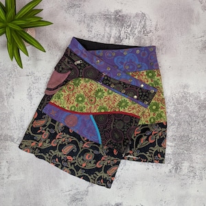 Peut inclure: Jupe patchwork avec différents tissus à motifs, notamment du violet, du vert et du noir. La jupe a une conception asymétrique avec une fermeture portefeuille et des boutons métalliques. Motifs : cachemire et floral. Longueur d'environ 40 cm.