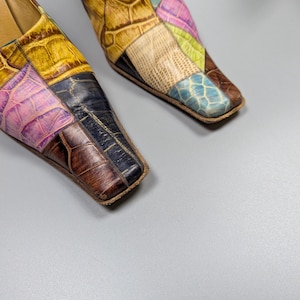 May include: A pair of colorful patchwork leather mules. The shoes feature a square toe and a low heel. The patchwork design includes shades of yellow, pink, blue, and brown, creating a unique and eye-catching pattern.