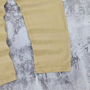 May include: A pair of solid tan trousers featuring a straight-leg cut and a smooth, matte fabric finish. The pants are shown from the waist down, highlighting the clean, unadorned design of the legs and the simple, straight hemline at the bottom.