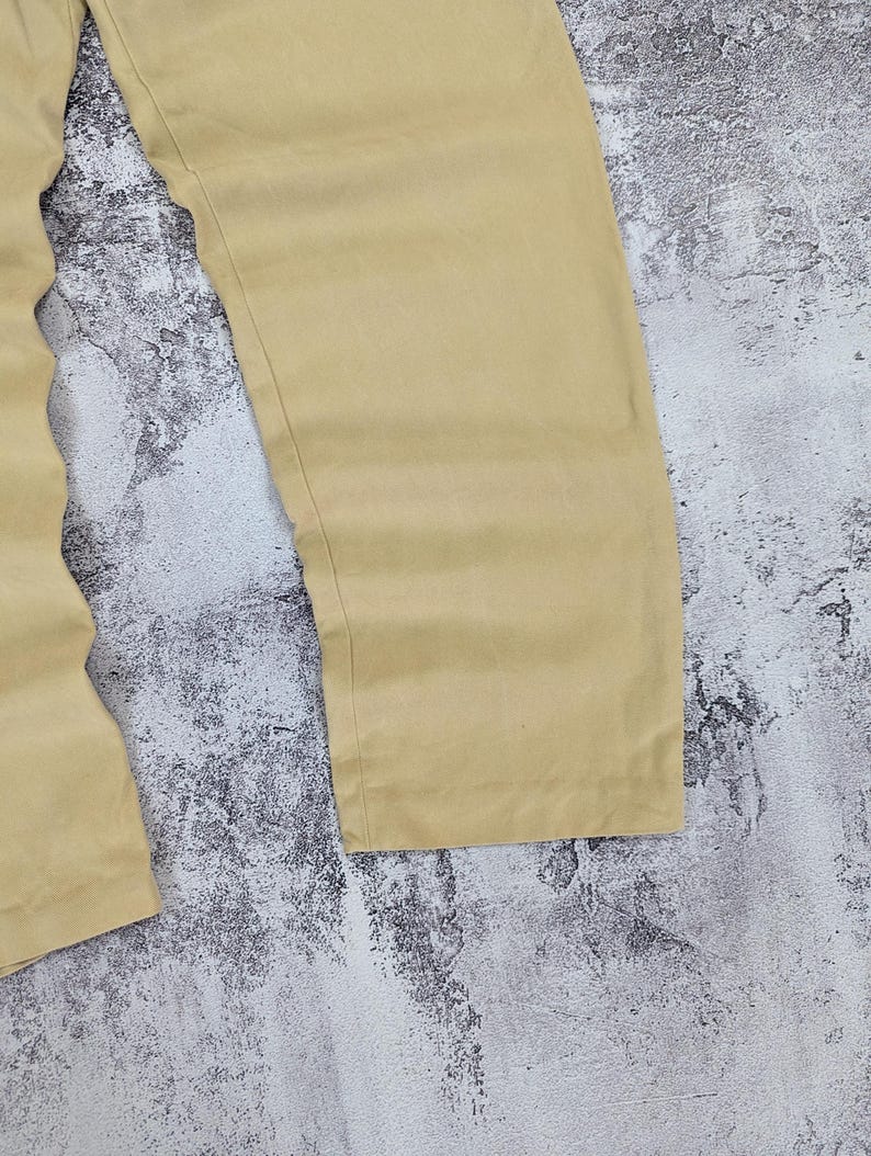 May include: A pair of solid tan trousers featuring a straight-leg cut and a smooth, matte fabric finish. The pants are shown from the waist down, highlighting the clean, unadorned design of the legs and the simple, straight hemline at the bottom.
