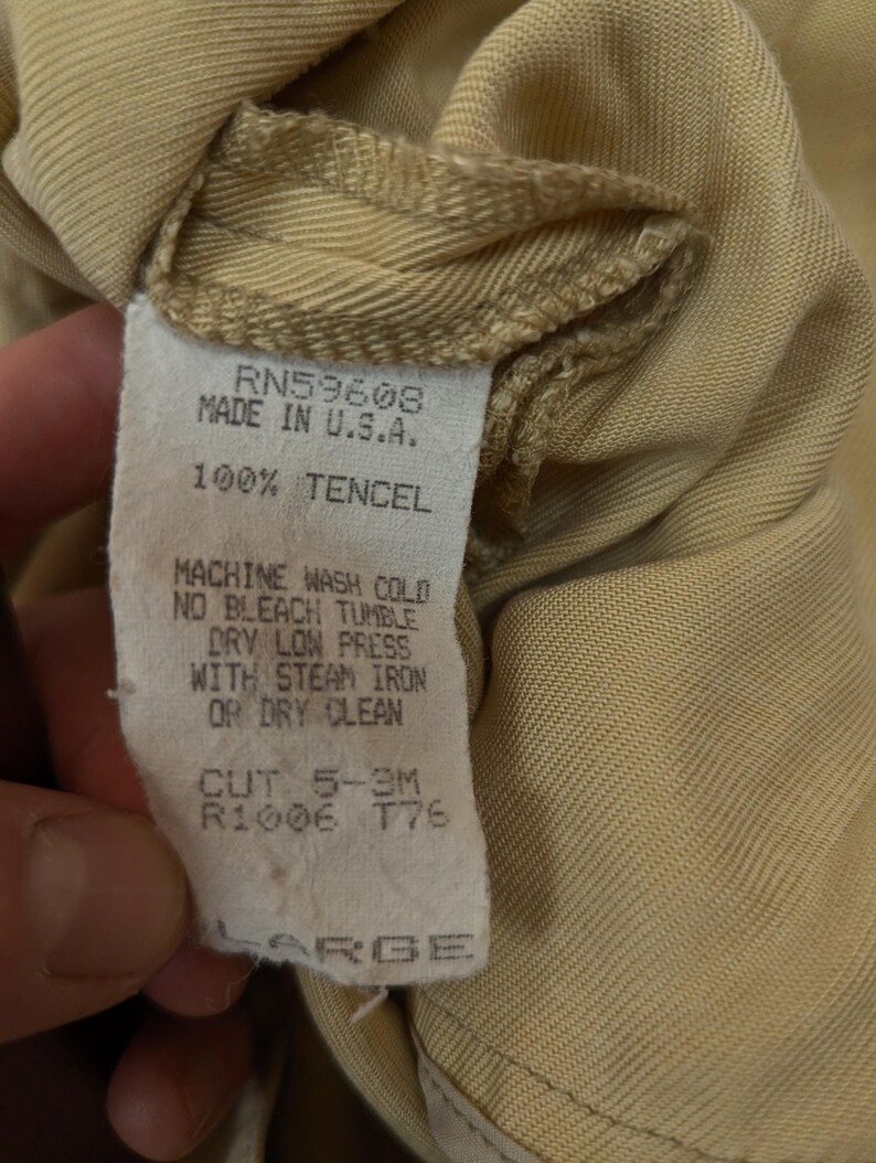 May include: A tan-colored garment tag featuring the text RN59608, MADE IN U.S.A., 100% TENCEL, MACHINE WASH COLD, NO BLEACH, TUMBLE DRY LOW, PRESS WITH STEAM IRON OR DRY CLEAN, CUT 5-3M, R1006, T76, and the size label LARGE in capital letters.