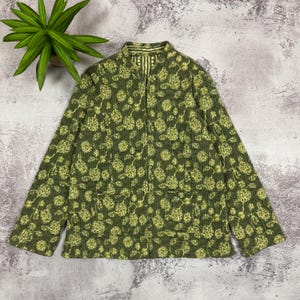 May include: A long-sleeved, quilted jacket in olive green featuring a repeating pattern of light yellow floral motifs. The jacket has a mandarin collar, a front button closure, and two square patch pockets on the lower front section.