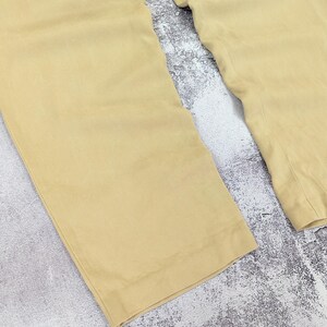 May include: A pair of light tan trousers featuring a wide-leg silhouette with straight hems. The fabric has a smooth, solid-colored appearance with visible vertical stitching along the inner seams and a clean, finished edge at the bottom of each leg.