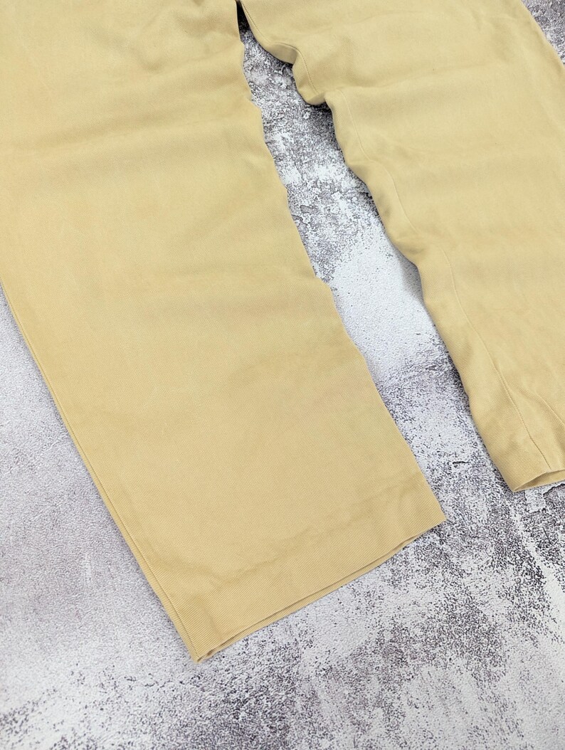 May include: A pair of light tan trousers featuring a wide-leg silhouette with straight hems. The fabric has a smooth, solid-colored appearance with visible vertical stitching along the inner seams and a clean, finished edge at the bottom of each leg.