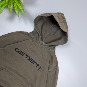 Puede incluir: Sudadera con capucha Carhartt verde oliva con bolsillo delantero y capucha. El logotipo de Carhartt est&aacute; impreso en negro en el pecho. La sudadera con capucha est&aacute; hecha de un material suave y duradero.