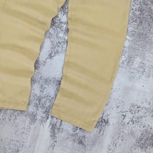 May include: A pair of light tan trousers featuring a straight-leg cut and a smooth, solid-colored fabric finish. The pants are shown from the waist down, displaying the full length of the legs with clean, simple seams and a consistent light beige tone.