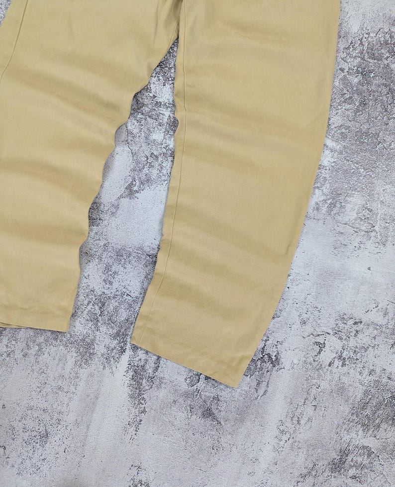 May include: A pair of light tan trousers featuring a straight-leg cut and a smooth, solid-colored fabric finish. The pants are shown from the waist down, displaying the full length of the legs with clean, simple seams and a consistent light beige tone.