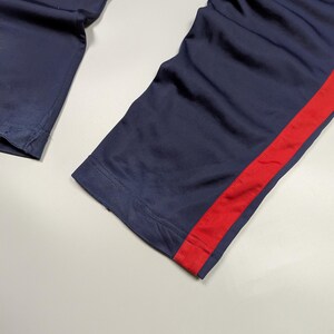 May include: Navy blue athletic trousers with a bold red stripe along the side. The fabric looks smooth, possibly synthetic. The image is a close-up of the lower part of the trousers.