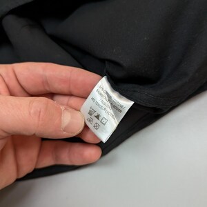 Puede incluir: Una prenda negra con una etiqueta blanca. La etiqueta muestra la composici&oacute;n de la tela: 54% Algod&oacute;n, 46% Tencel Lyocell. Tambi&eacute;n se ven instrucciones de lavado.