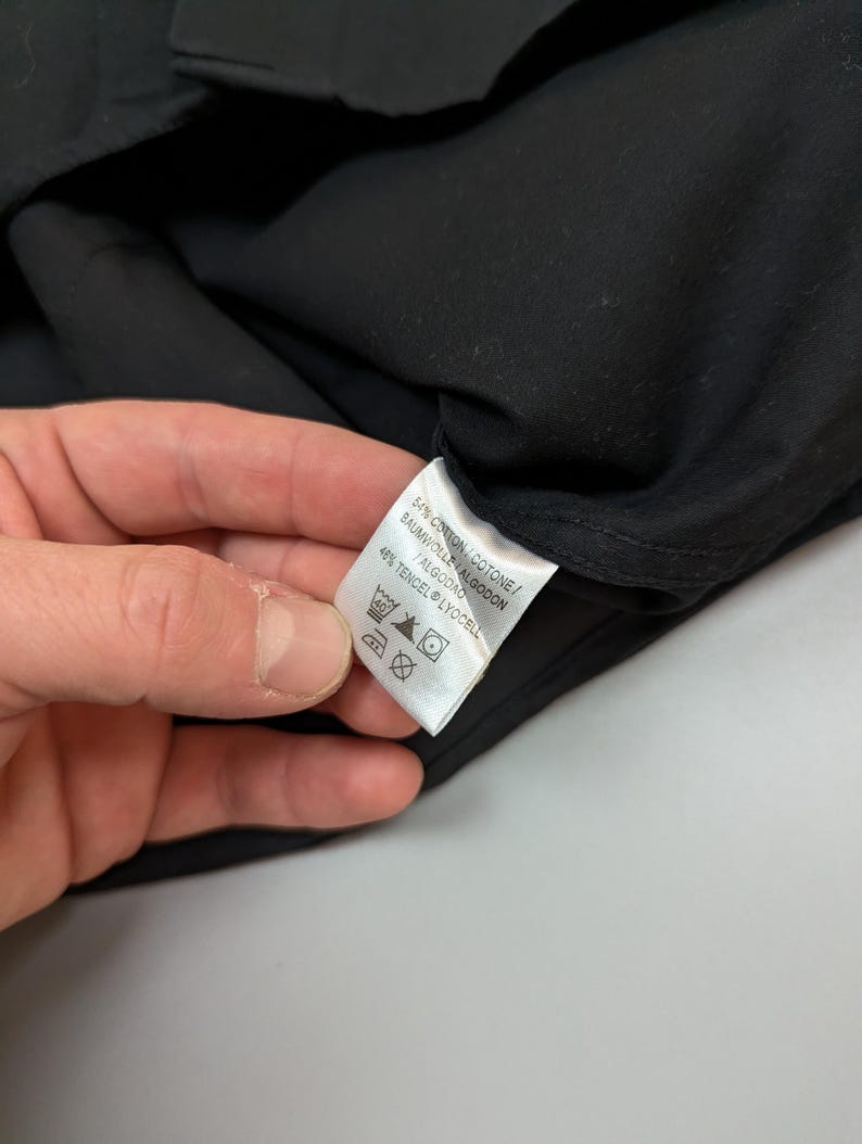 Puede incluir: Una prenda negra con una etiqueta blanca. La etiqueta muestra la composici&oacute;n de la tela: 54% Algod&oacute;n, 46% Tencel Lyocell. Tambi&eacute;n se ven instrucciones de lavado.