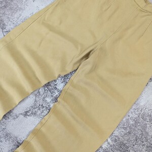 May include: A pair of solid light tan trousers featuring a high-waisted design with a visible elastic waistband at the top. The pants have a clean, straight-leg cut with subtle vertical seam detailing running down the front of each leg.
