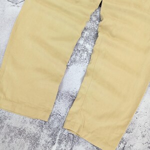 May include: A pair of light yellow trousers featuring a wide-leg silhouette and a clean, unadorned hemline. The fabric has a smooth, matte texture and a consistent solid color throughout, showcasing the straight-cut design of the pant legs.