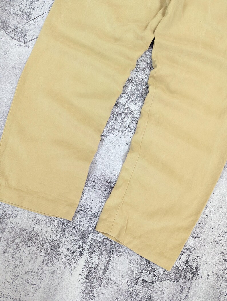 May include: A pair of light yellow trousers featuring a wide-leg silhouette and a clean, unadorned hemline. The fabric has a smooth, matte texture and a consistent solid color throughout, showcasing the straight-cut design of the pant legs.