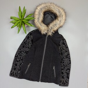 May include: A dark gray hooded jacket with a faux fur trim around the hood. The sleeves feature a black and gray floral pattern. The jacket has a full-length zipper and two front pockets. A plant is visible in the background.