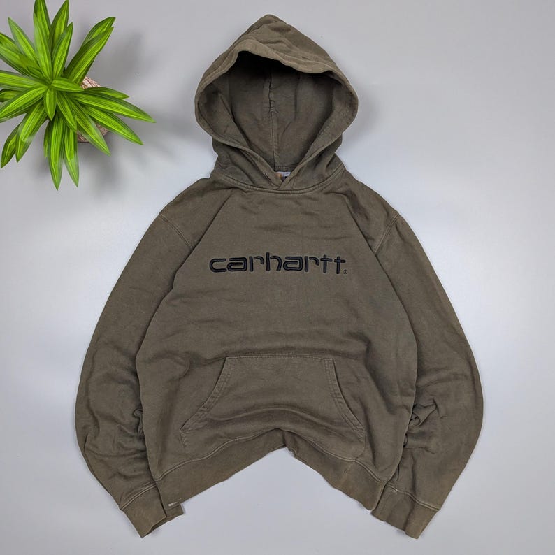 Puede incluir: Sudadera con capucha Carhartt verde oliva con capucha y bolsillo delantero. El nombre de la marca est&aacute; bordado en negro en el pecho. La sudadera est&aacute; hecha de un material suave y c&oacute;modo.
