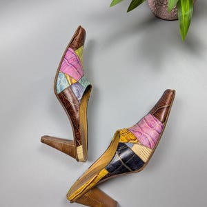 May include: A pair of vintage patchwork leather mules with pointed toes and wooden heels. The uppers feature a mix of colors including pink, blue, yellow, and brown. The heels are approximately 3 inches tall.