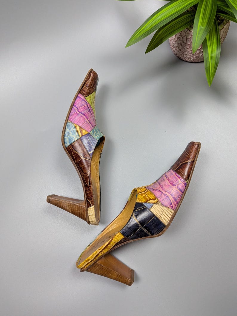 May include: A pair of vintage patchwork leather mules with pointed toes and wooden heels. The uppers feature a mix of colors including pink, blue, yellow, and brown. The heels are approximately 3 inches tall.