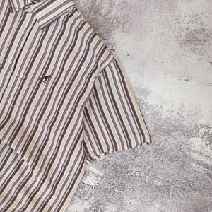 K&ouml;nnte beinhalten: Kurz&auml;rmeliges Button-Down-Hemd mit vertikalen Streifen in Braun-, Beige- und Graut&ouml;nen. Das Hemd hat ein kleines K&auml;nguru-Logo auf der Brust. Das Hemd h&auml;ngt an einem schwarzen Kleiderb&uuml;gel.