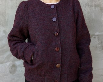 May include: A burgundy-colored jacket with a round neckline and long sleeves. The jacket has a textured appearance and features four large, round buttons down the front. The jacket has two pockets and is made of a woven material.