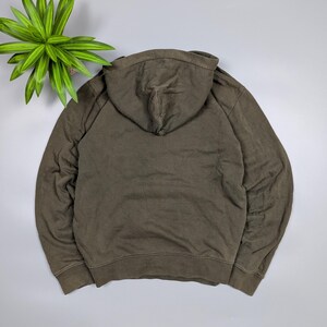 Puede incluir: Una sudadera con capucha verde oliva descolorida, vista desde atr&aacute;s, con capucha y mangas largas. La tela parece suave y c&oacute;moda. La sudadera es de color liso y tiene un corte informal.