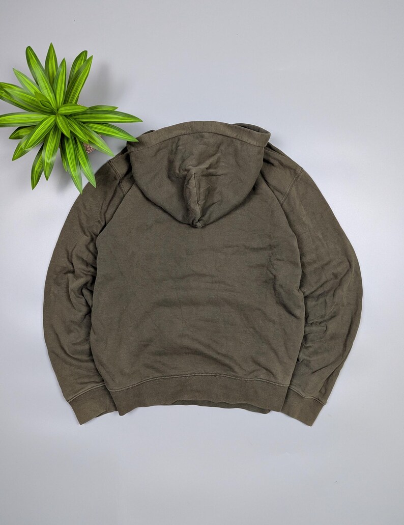 Puede incluir: Una sudadera con capucha verde oliva descolorida, vista desde atr&aacute;s, con capucha y mangas largas. La tela parece suave y c&oacute;moda. La sudadera es de color liso y tiene un corte informal.