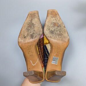 May include: A pair of colorful high-heeled shoes with square toes. The soles are worn, and the heels are a dark brown. The uppers feature a patchwork design with various colors and patterns. The size is 37 1/2.