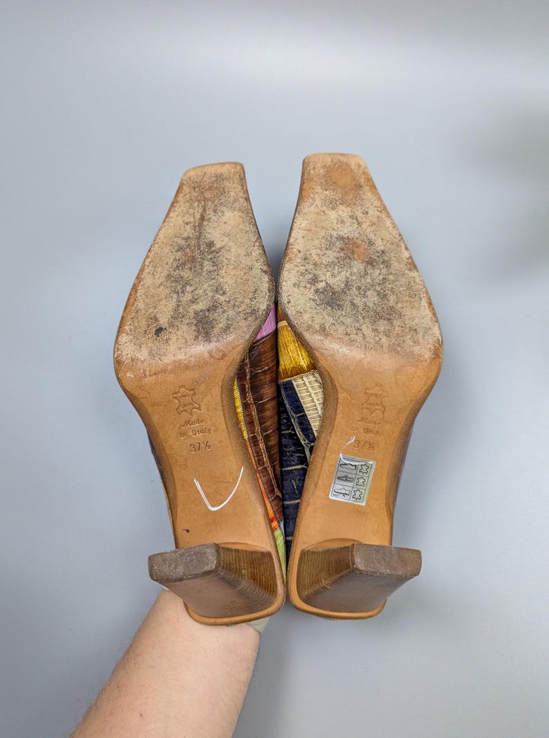 May include: A pair of colorful high-heeled shoes with square toes. The soles are worn, and the heels are a dark brown. The uppers feature a patchwork design with various colors and patterns. The size is 37 1/2.