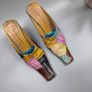 May include: A pair of Gianmarco Lorenzi patchwork leather mules. The shoes feature a variety of colors including pink, yellow, brown, and blue. The heels are low and the shoes have a pointed toe.