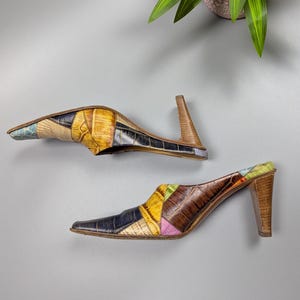 May include: A pair of patchwork leather mules with pointed toes and wooden heels. The shoes feature a variety of colors including yellow, blue, brown, and pink. The heels are approximately 3 inches high.