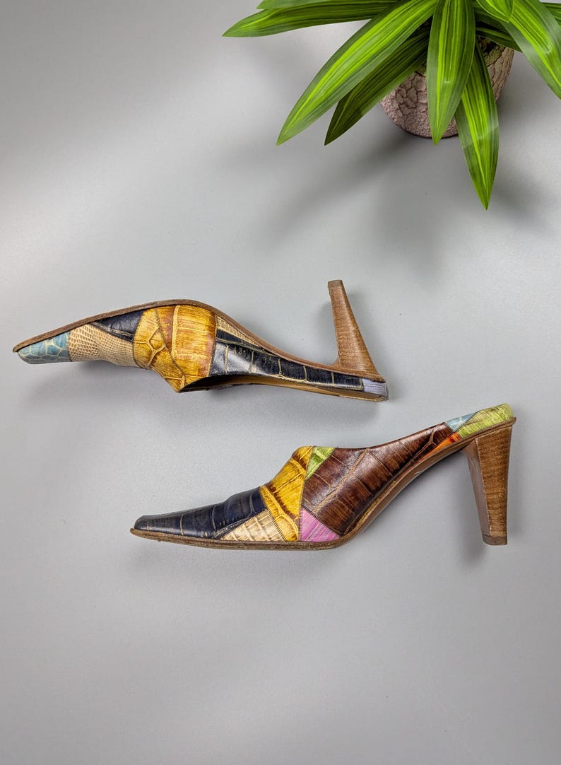 May include: A pair of patchwork leather mules with pointed toes and wooden heels. The shoes feature a variety of colors including yellow, blue, brown, and pink. The heels are approximately 3 inches high.