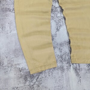 May include: A pair of light tan trousers featuring a straight-leg cut with visible vertical seam detailing running down the front of each leg. The fabric has a smooth, matte finish and the garment is presented in a simple, clean design.